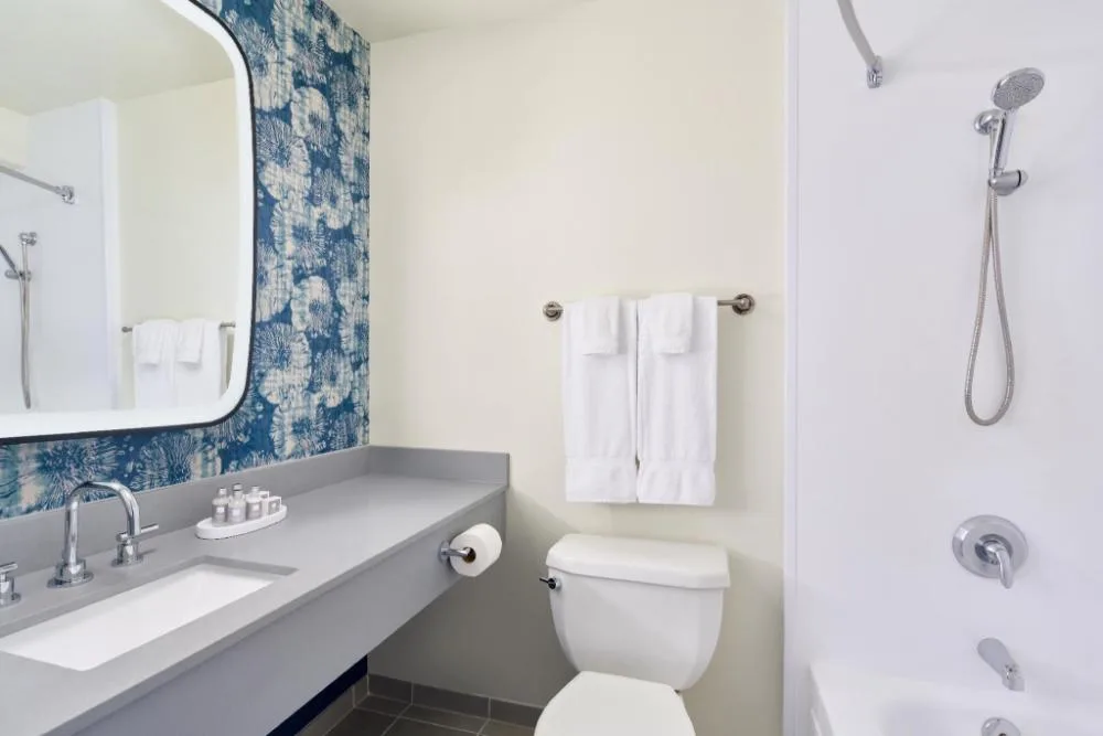 Standard room bathroom with vanity, toilet, towels, and shower-tub at Waikiki Malia.