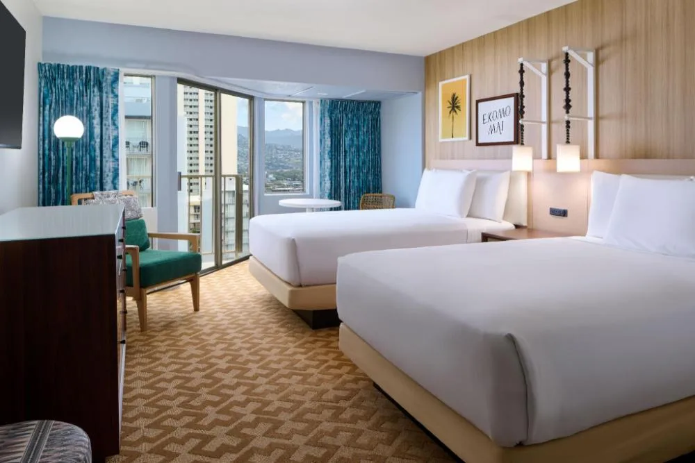 Standard room with two beds, balcony doors, and seating at Waikiki Malia.