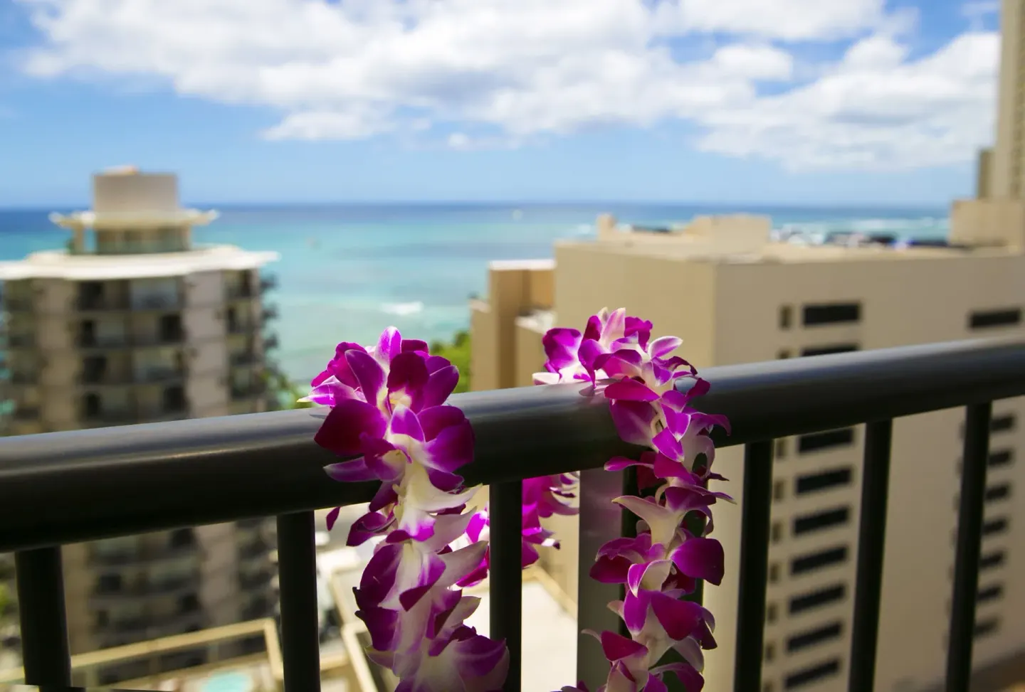 Purple lei flowers on a balcony railing with ocean and city views at Waikiki Resort Hotel.