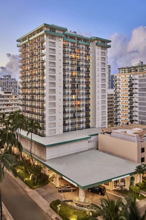 Tall exterior tower with balconies and entrance canopy at Waikiki Resort Hotel at dusk.