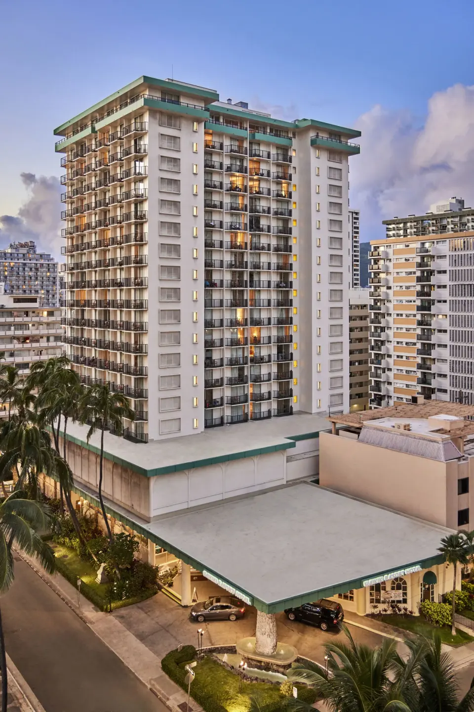 Tall exterior tower with balconies and entrance canopy at Waikiki Resort Hotel at dusk.