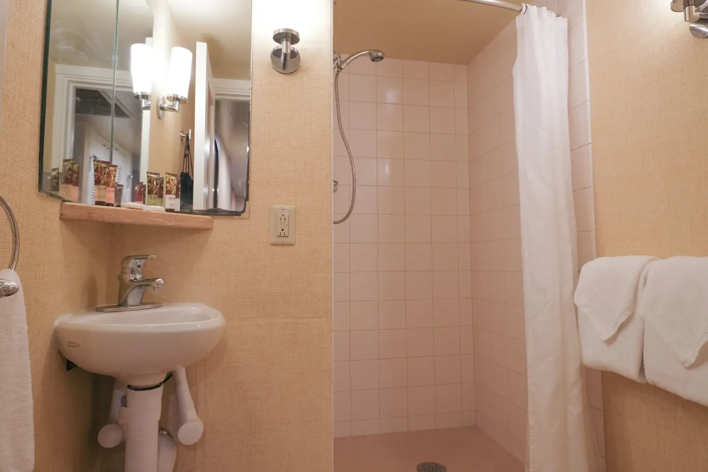 Compact guest bathroom with pedestal sink and curtained shower at Waikiki Resort Hotel.