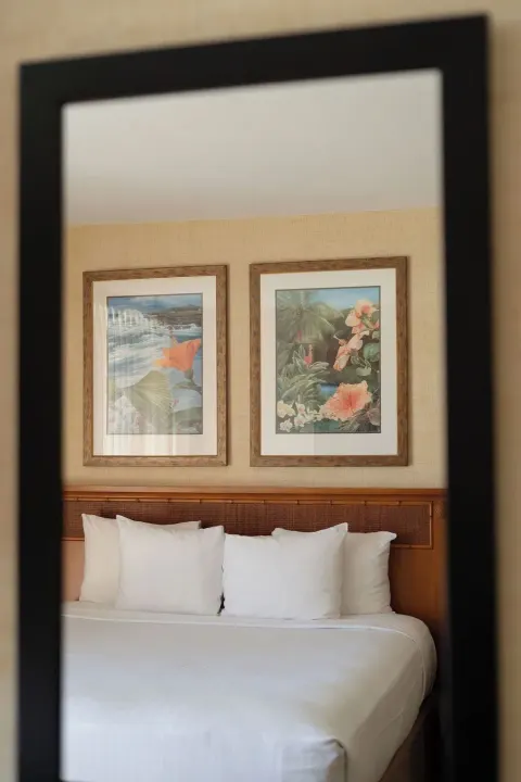 Guest room bed reflected in a mirror with framed tropical artwork at Waikiki Resort Hotel.