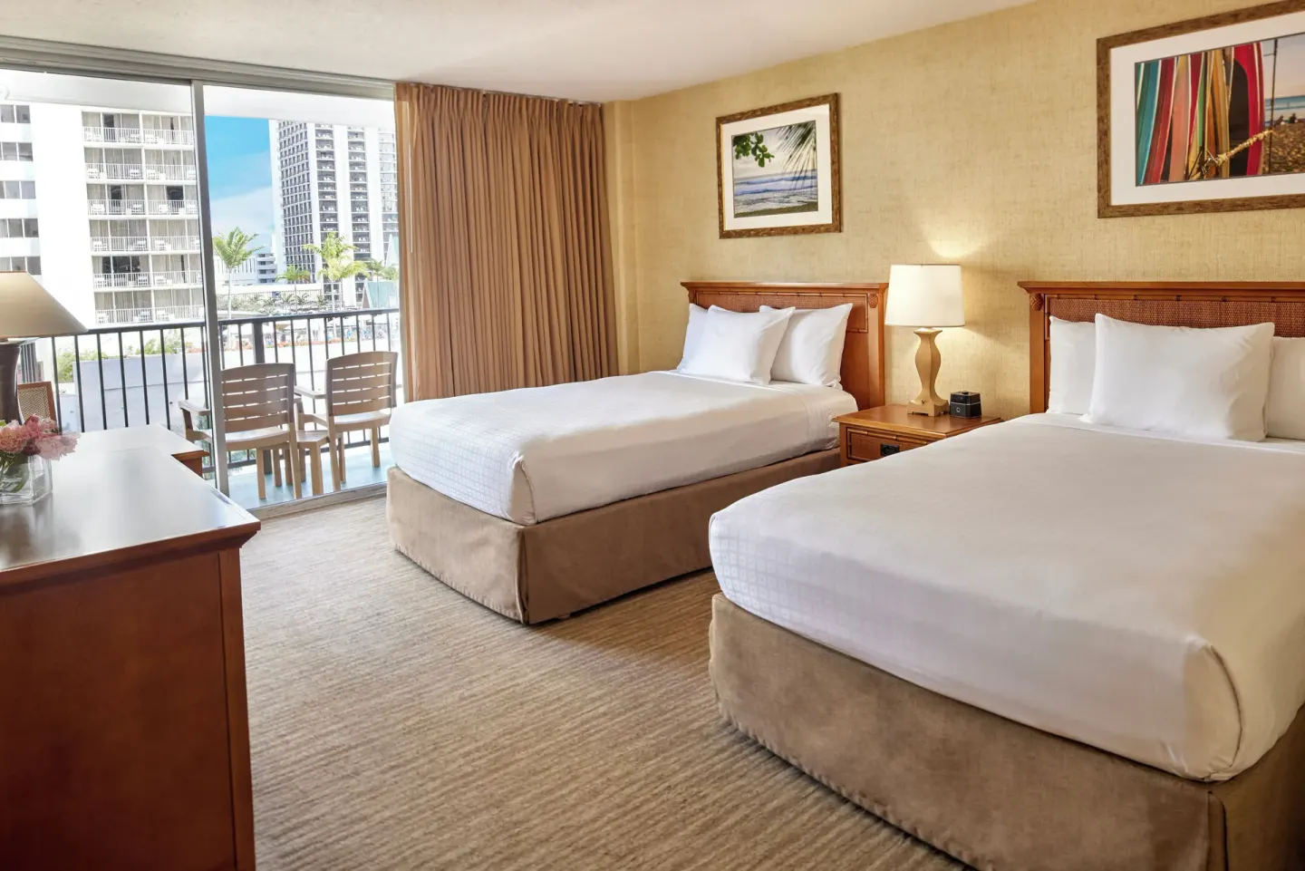 Guest room with two beds, balcony chairs, and city buildings visible at Waikiki Resort Hotel.