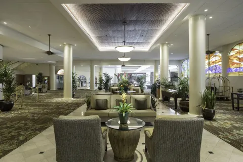 Lobby lounge area at Waikiki Resort Hotel with wicker chairs, columns, plants, and stained-glass windows.