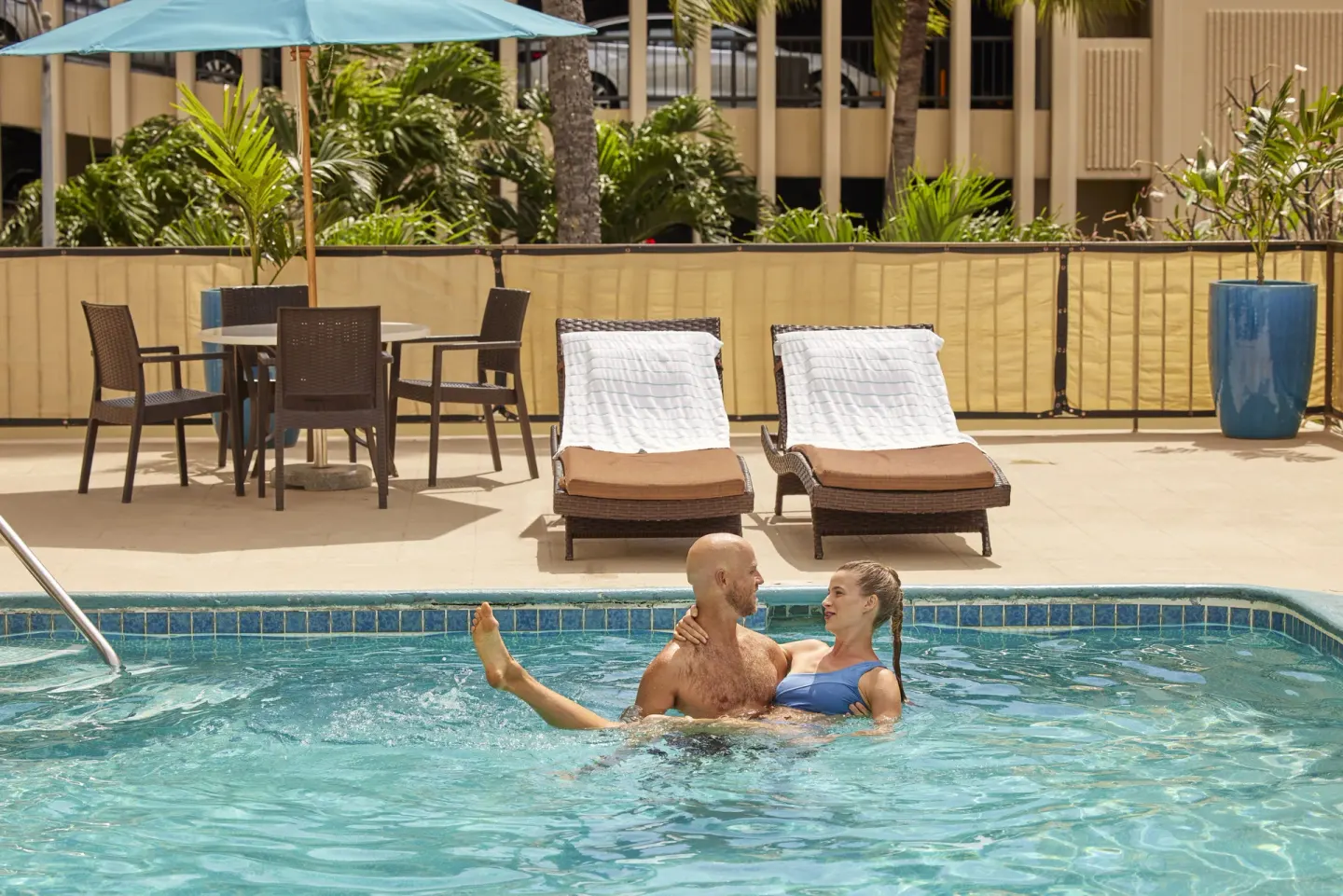 Outdoor pool with two guests in the water and lounge seating at Waikiki Resort Hotel.