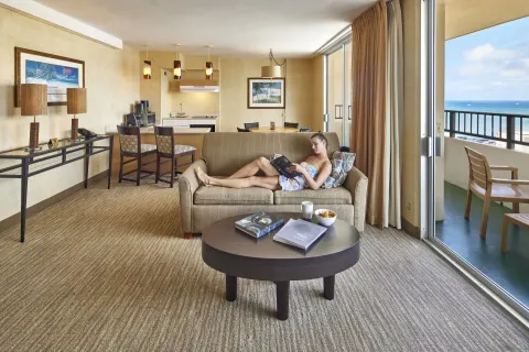 Suite living area with sofa, kitchenette, balcony, and ocean view at Waikiki Resort Hotel.