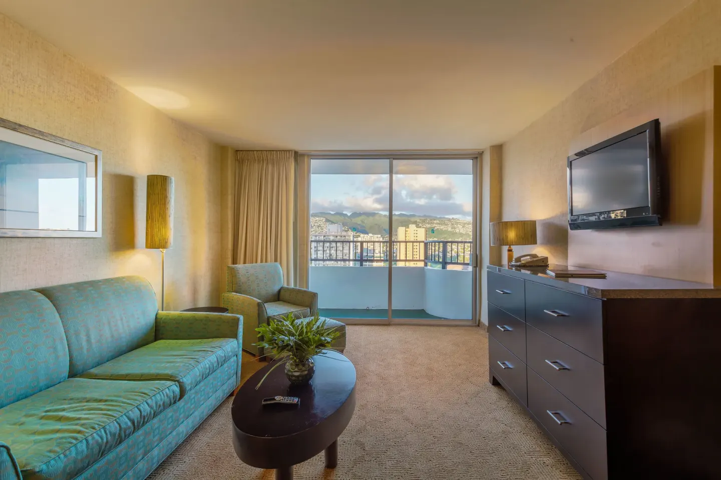 Suite sitting area with sofa, balcony, dresser, and mountain view at Waikiki Resort Hotel.