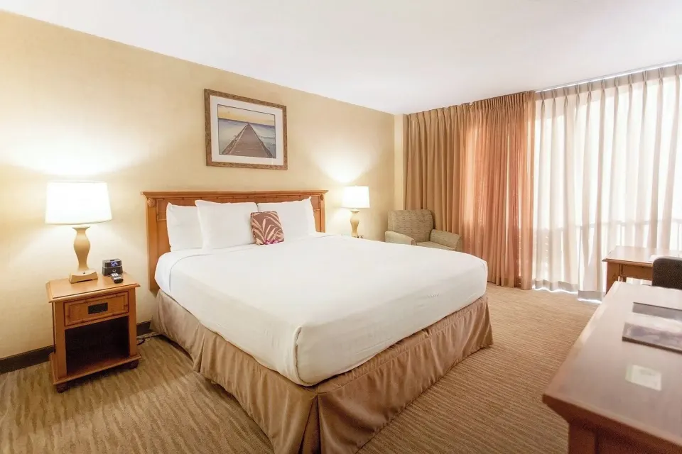 City View room with king bed, lamps, armchair, and curtained balcony at Waikiki Resort Hotel.