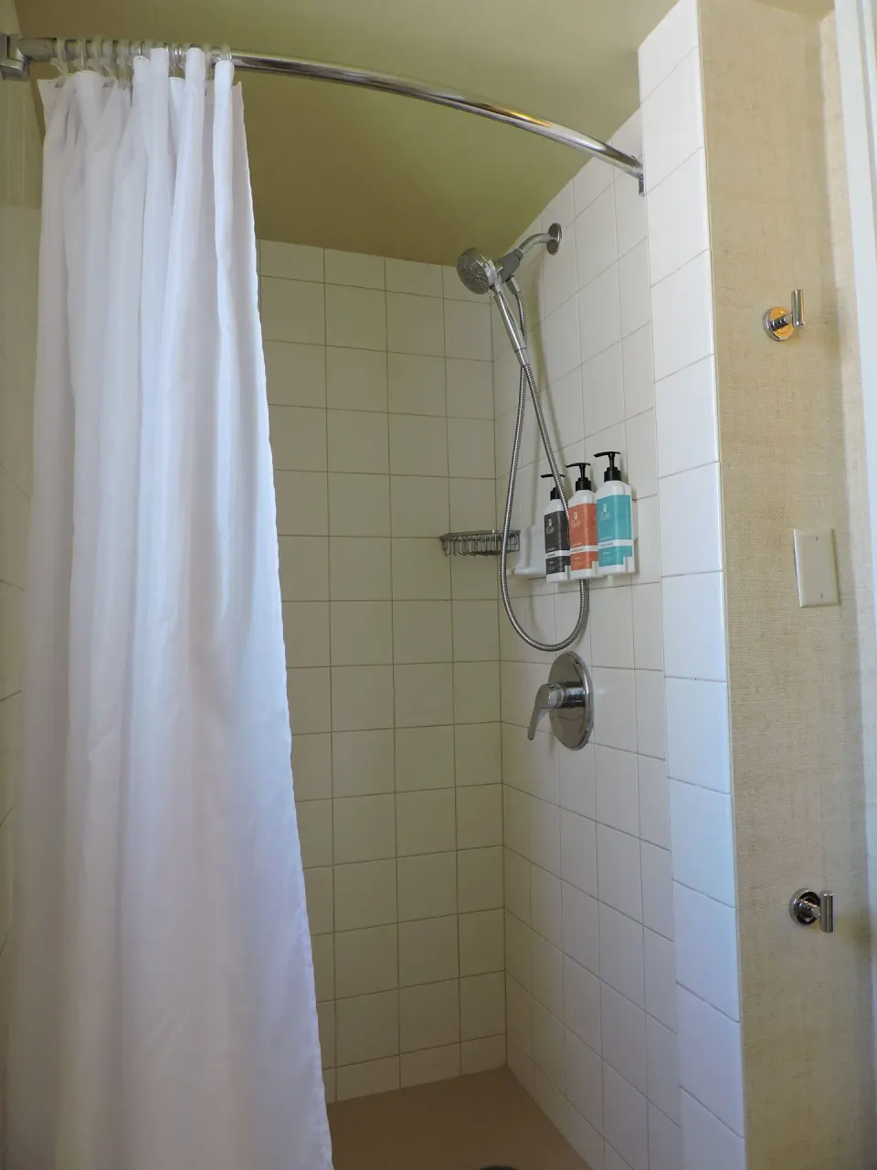 Guest room shower with white tile and curtain at Waikiki Resort Hotel.