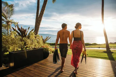 Couple carries swim fins toward the sunset ocean at Wailea Beach Resort - Marriott, Maui.