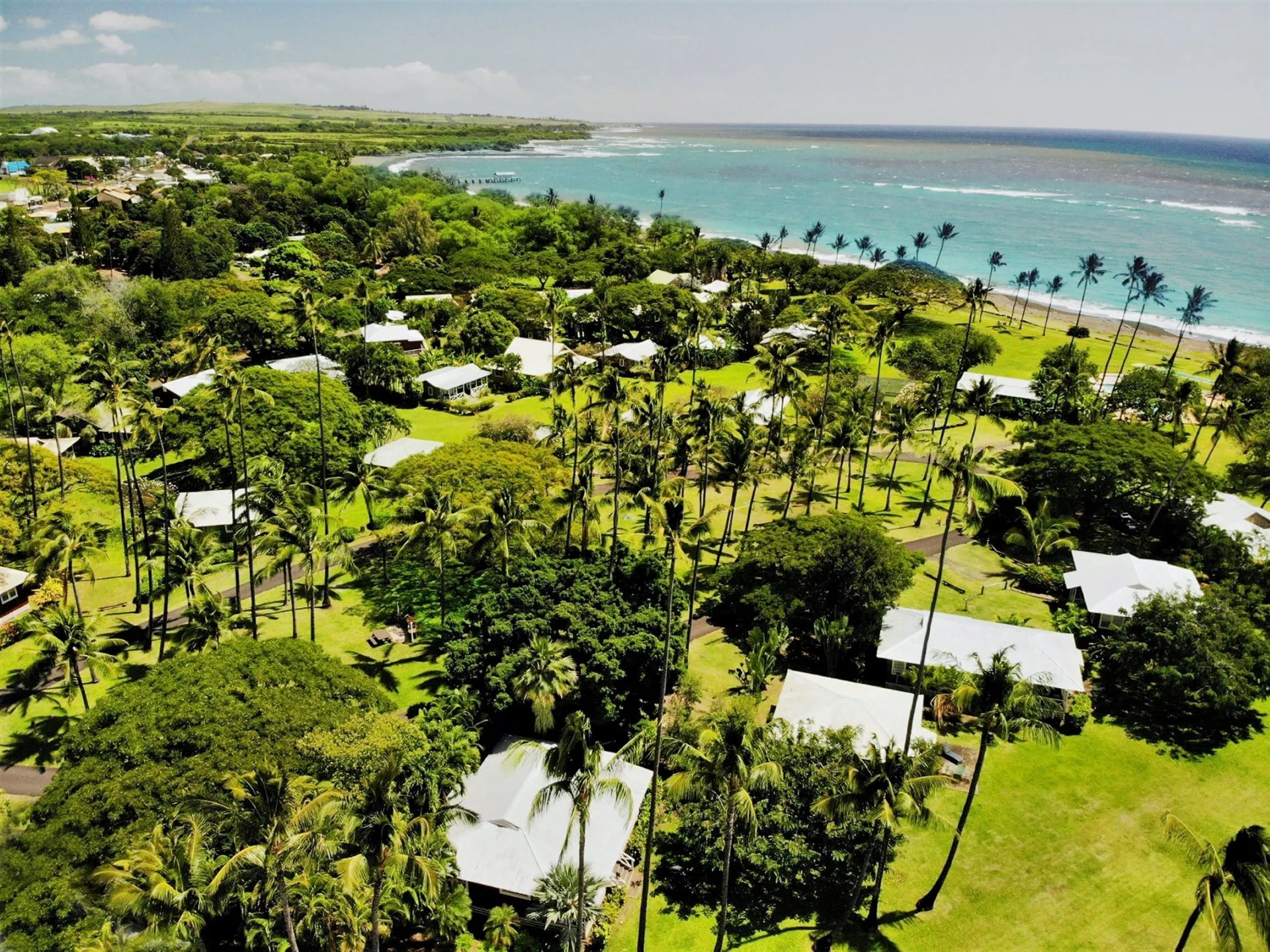 Aerial view of cottages, palms, lawns, and shoreline at Waimea Plantation Cottages.