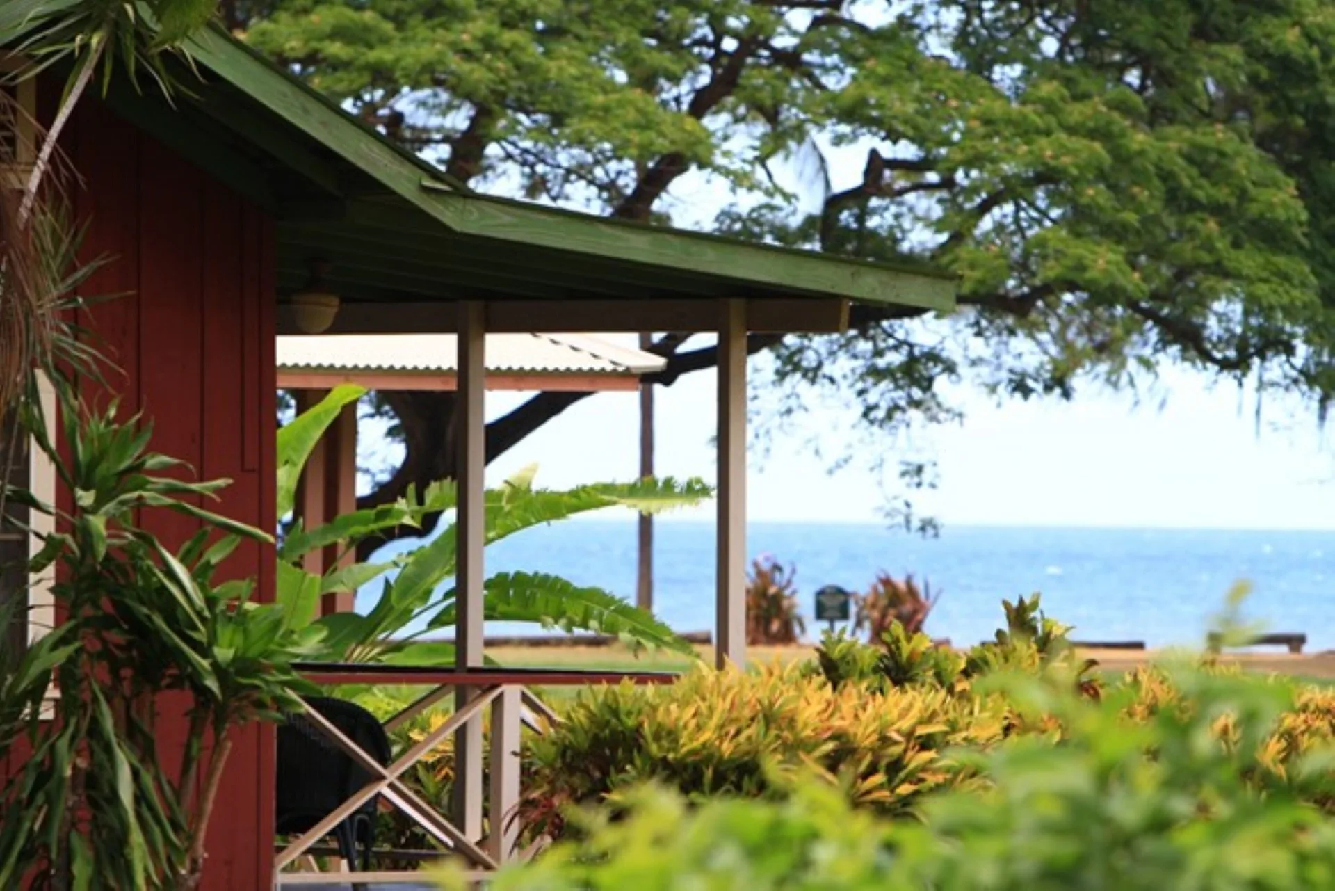 Cottage porch framed by tropical plants with the ocean beyond at Waimea Plantation Cottages.