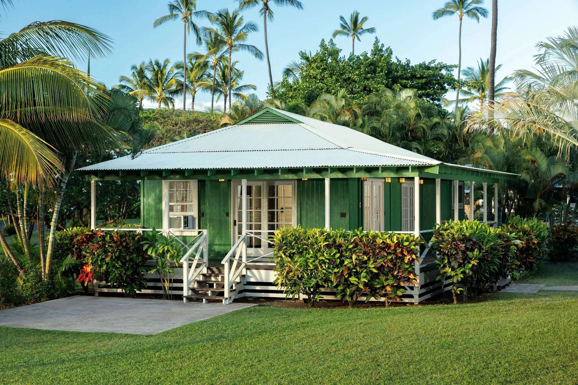 Green plantation cottage with porch and tropical hedges at Waimea Plantation Cottages.