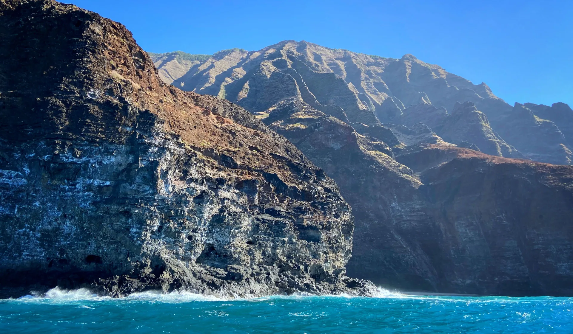 Ocean view of rugged Kauai cliffs near Waimea Plantation Cottages under a clear blue sky.