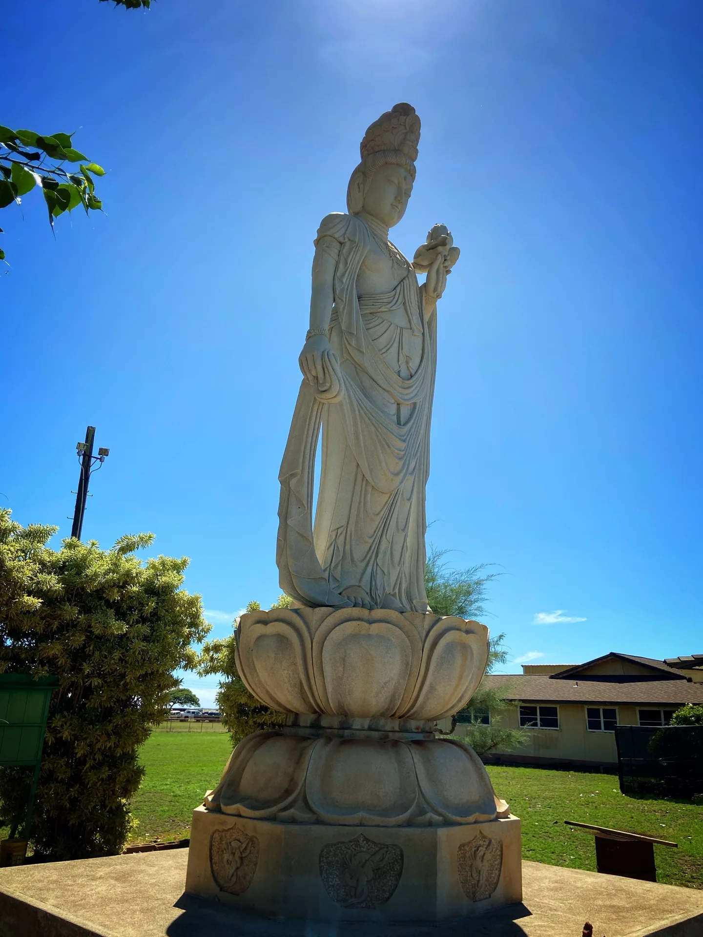 Outdoor stone statue on the lawn at Waimea Plantation Cottages beneath a bright blue sky.
