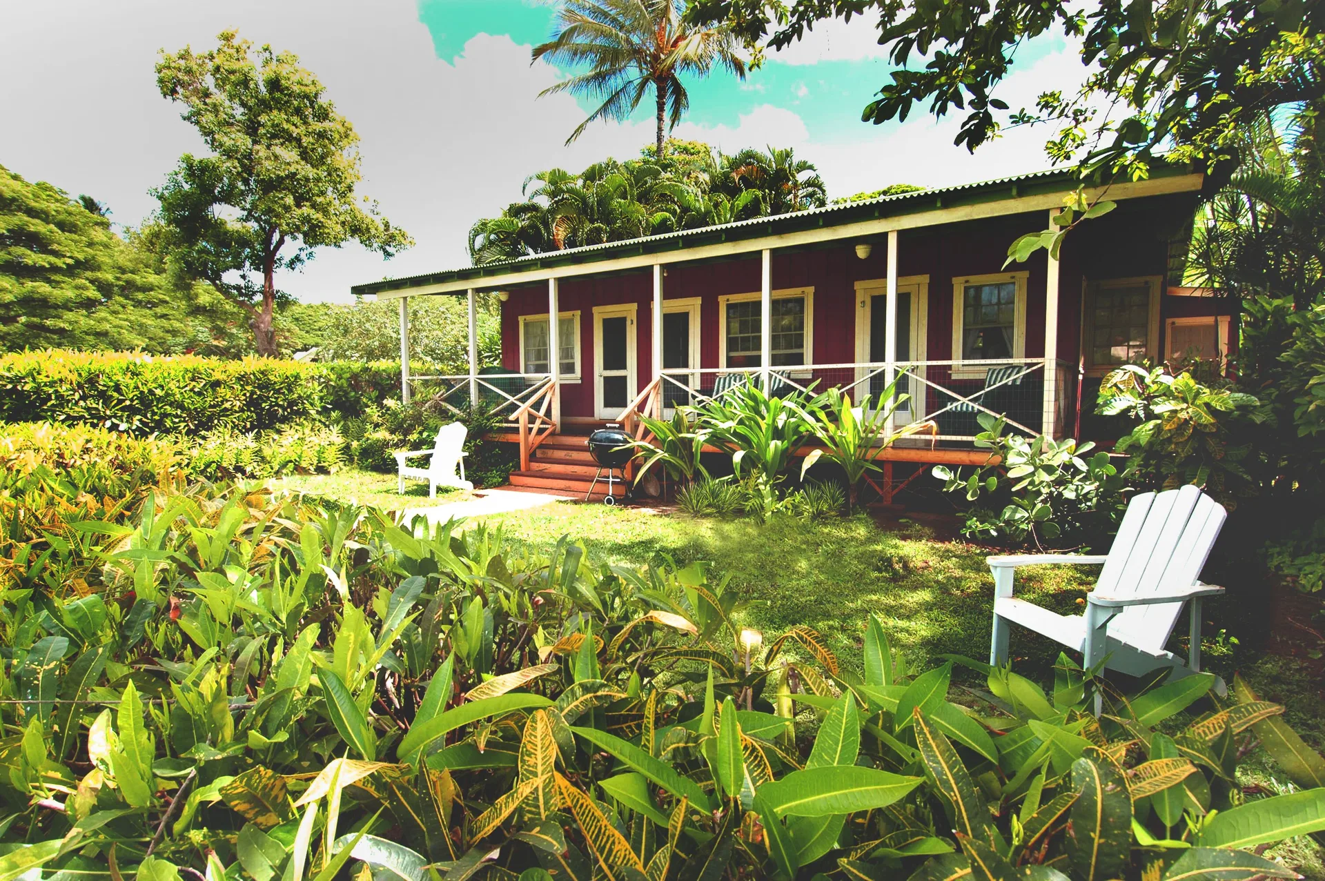 Red cottage with porch, garden chairs, and tropical landscaping at Waimea Plantation Cottages.