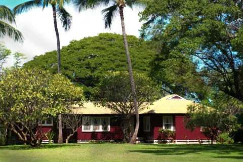 Red plantation cottage set on a broad lawn beneath palms at Waimea Plantation Cottages.