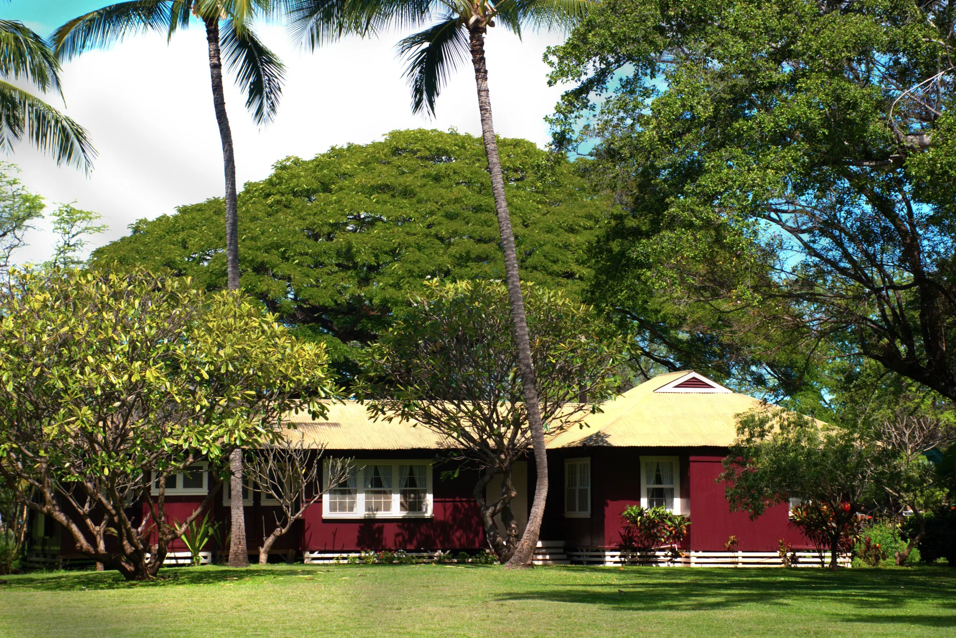 Red plantation cottage set on a broad lawn beneath palms at Waimea Plantation Cottages.
