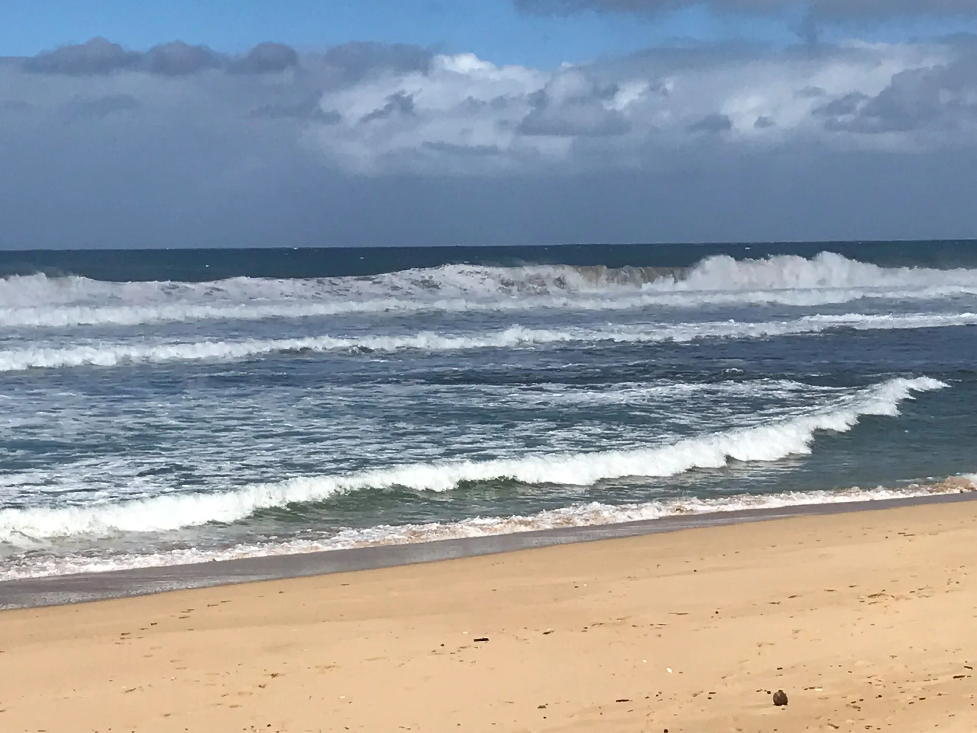 Sandy beach and breaking ocean waves near Waimea Plantation Cottages on a cloudy day.