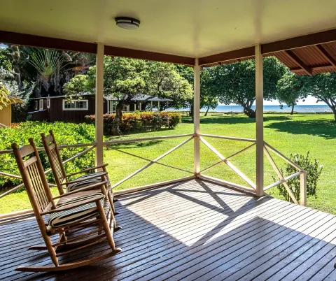 Coast Cottage porch with two rocking chairs and ocean beyond at Waimea Plantation Cottages.