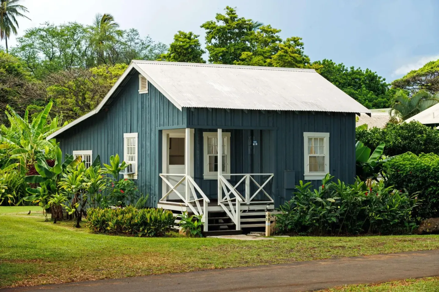 Blue garden-view cottage exterior with white porch railings and tropical landscaping at Waimea Plantation Cottages.