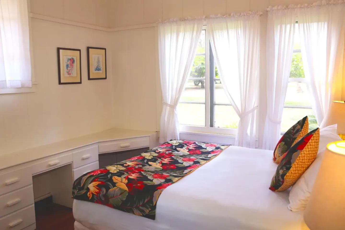 Garden-view cottage bedroom with bed, floral runner, desk, and curtained windows at Waimea Plantation Cottages.