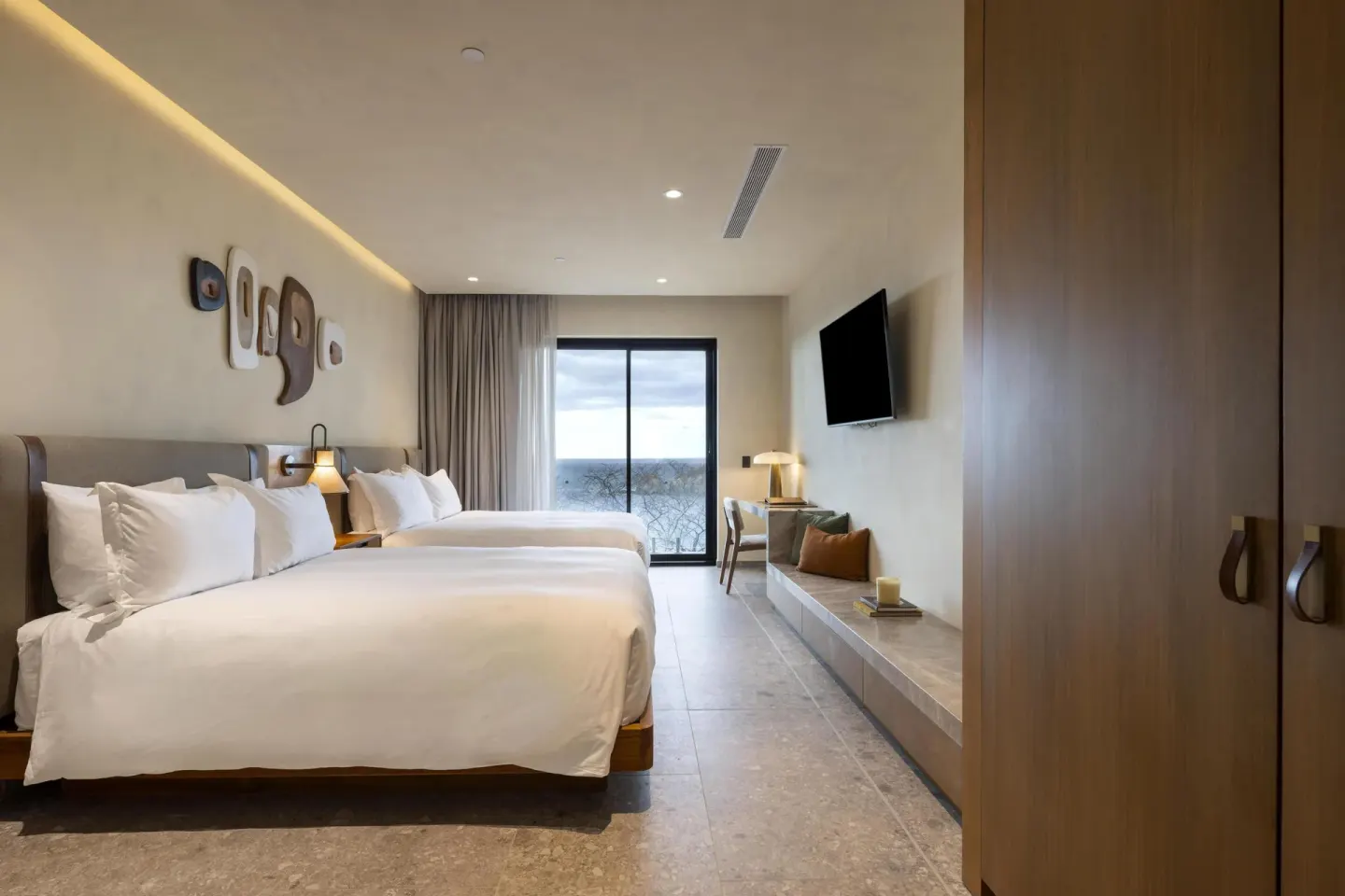 Two-bed guest room with balcony doors and wood wardrobe at Waldorf Astoria Costa Rica Punta Cacique.