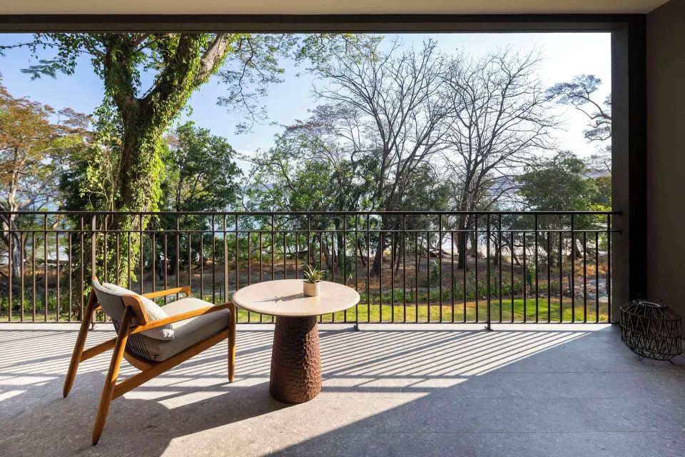 Bahia View room balcony with chair, table, trees, and water glimpses at Waldorf Astoria Costa Rica Punta Cacique.