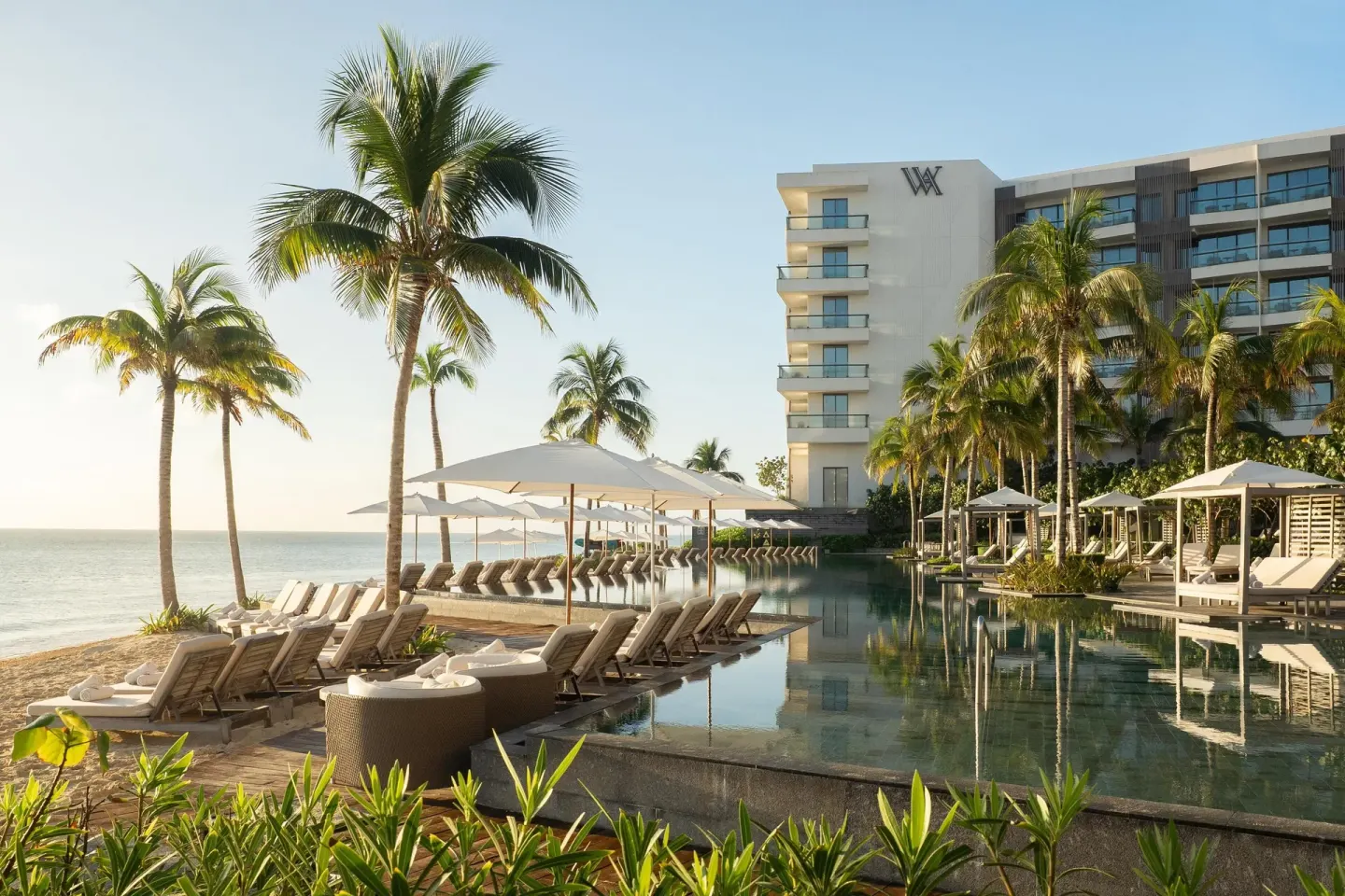 Beachfront pool with loungers, palms, and resort building at Waldorf Astoria Riviera Maya.