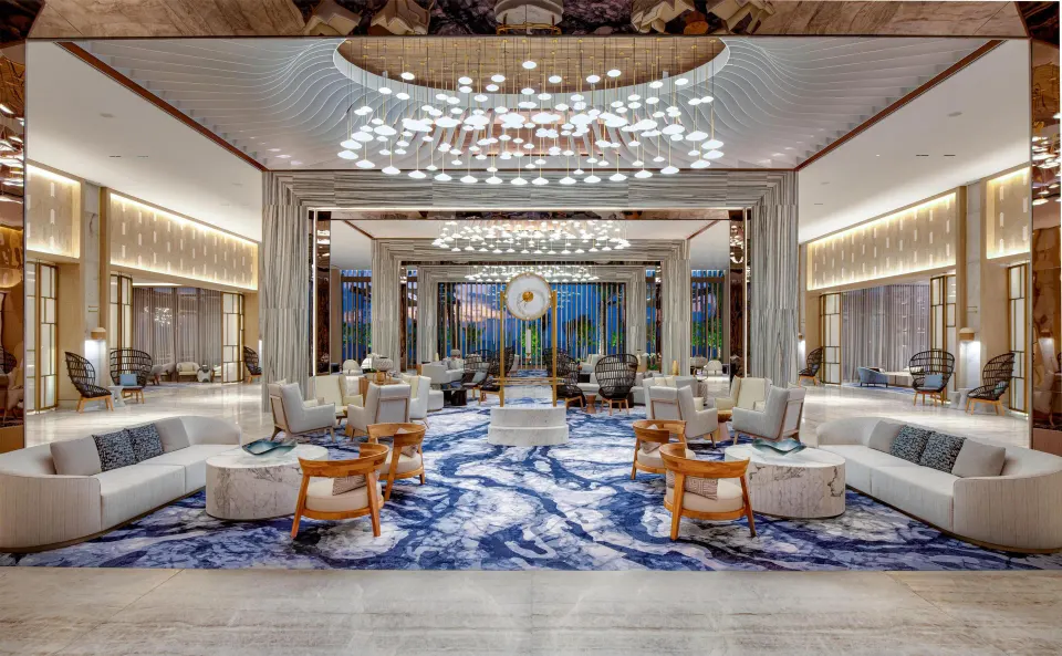Grand lobby lounge with blue patterned rug and chandeliers at Waldorf Astoria Riviera Maya.