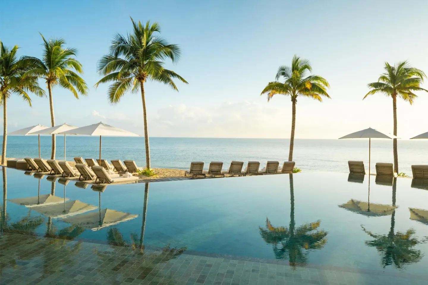 Infinity pool, palm trees, loungers, and ocean view at Waldorf Astoria Riviera Maya.