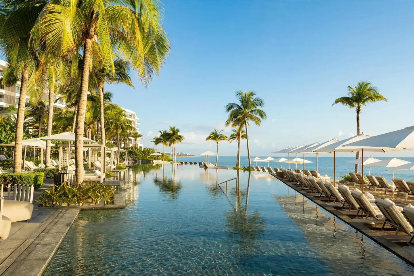 Long beachfront pool with palms, umbrellas, and loungers at Waldorf Astoria Riviera Maya.