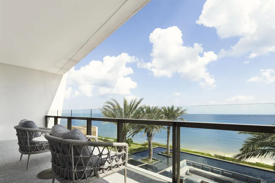 Ocean-view balcony with cushioned chairs and palm trees at Waldorf Astoria Riviera Maya.