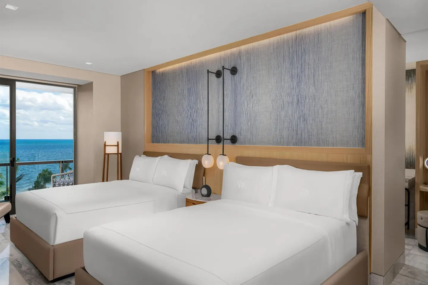 Guest room with two beds beside a window overlooking the ocean at Waldorf Astoria Riviera Maya.