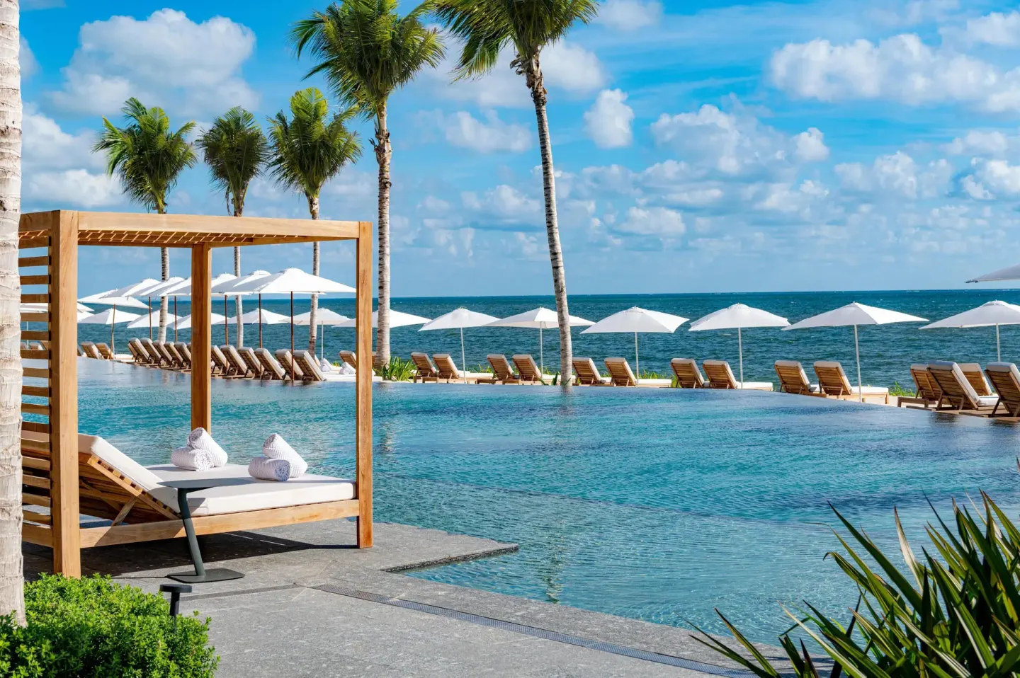Oceanfront pool with cabana, palms, umbrellas, and loungers at Waldorf Astoria Riviera Maya.