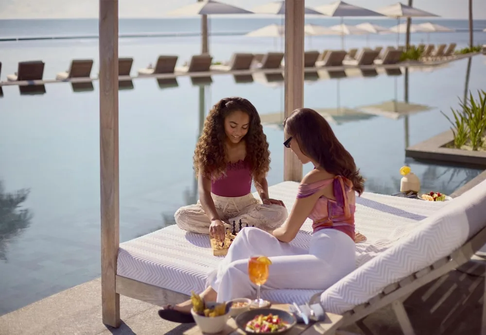 Guests playing chess on a poolside daybed at Waldorf Astoria Riviera Maya.