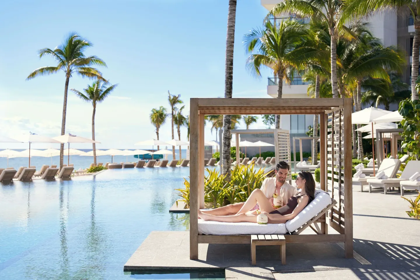 Couple lounges on a shaded poolside daybed at Waldorf Astoria Riviera Maya.