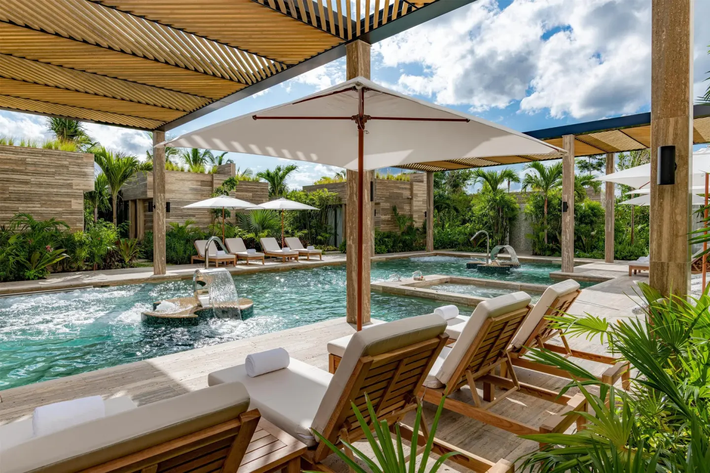 Shaded spa-style pool with loungers and umbrellas at Waldorf Astoria Riviera Maya.