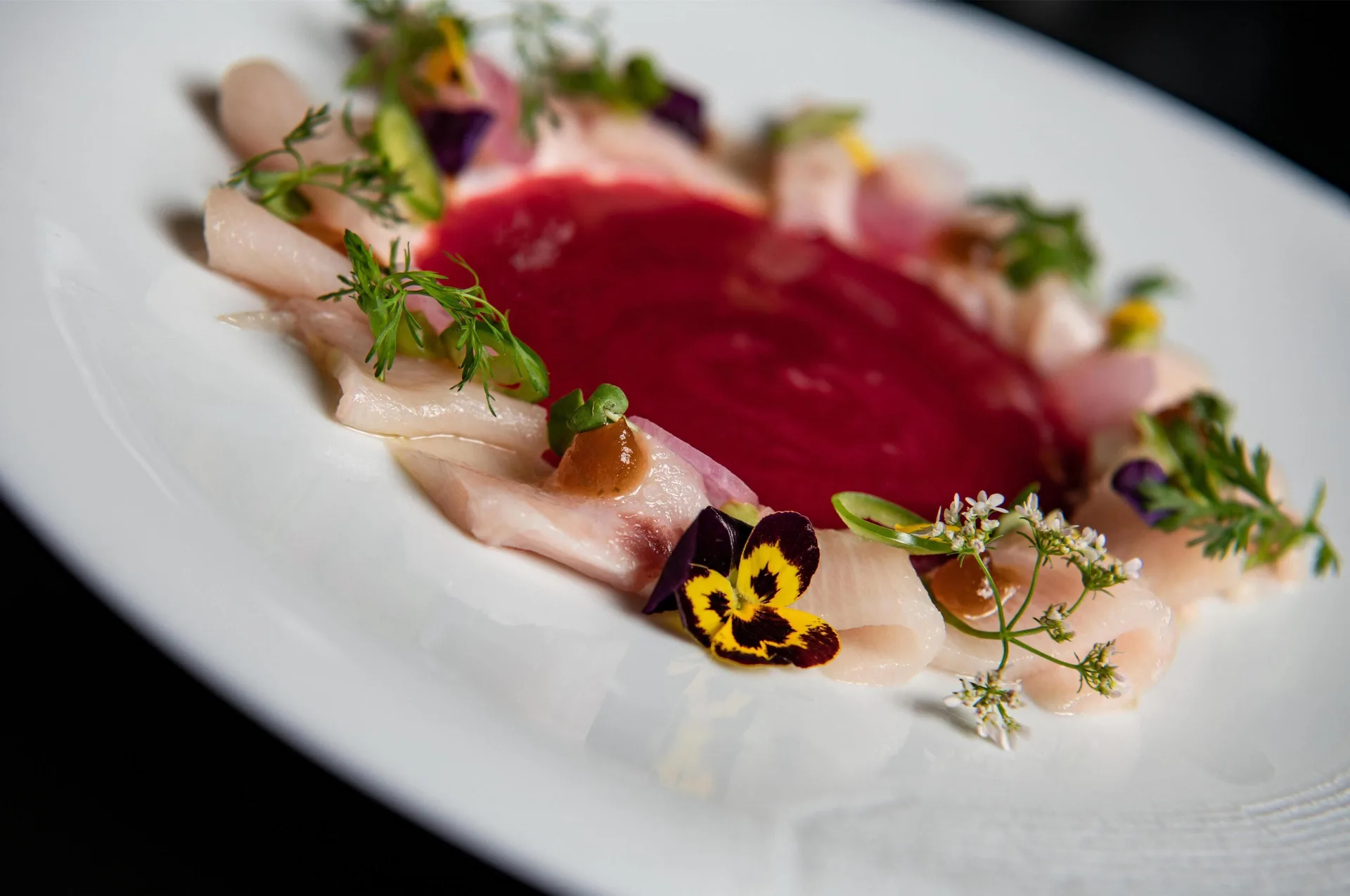 Plated seafood dish with red sauce and edible flowers at Waldorf Astoria Riviera Maya.