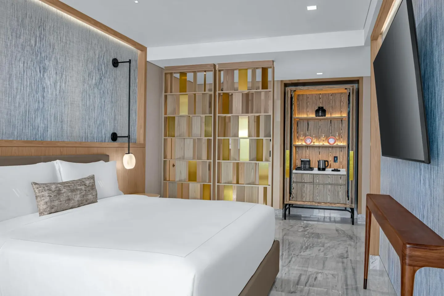 Deluxe Ocean View king bed with partition shelving and refreshment cabinet at Waldorf Astoria Riviera Maya.