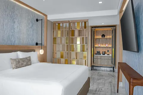 Deluxe Ocean View king bed with partition shelving and refreshment cabinet at Waldorf Astoria Riviera Maya.