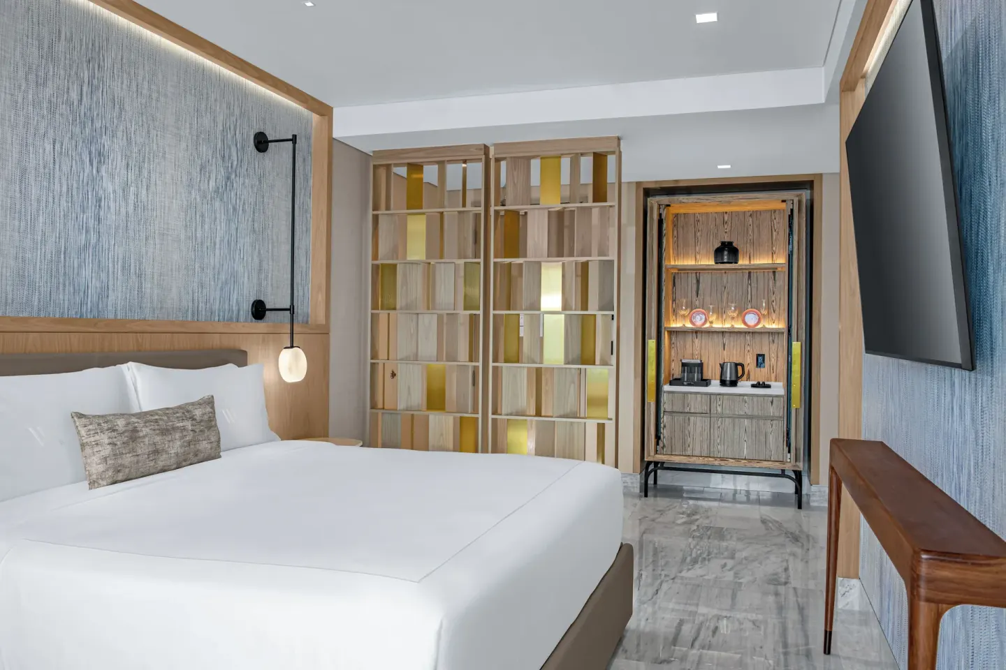 Deluxe Ocean View king bed with TV, shelving, and refreshment cabinet at Waldorf Astoria Riviera Maya.