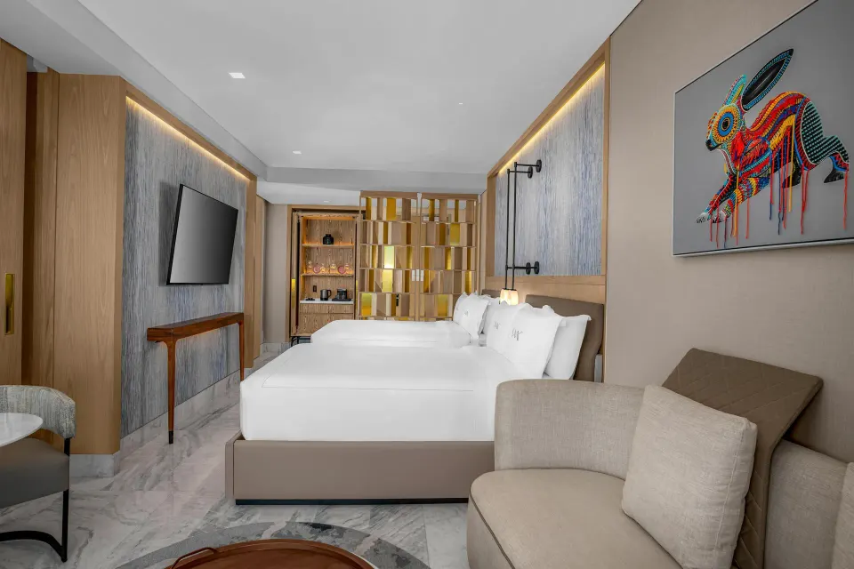 Deluxe Ocean View room with two queen beds, sofa, TV, and wall art at Waldorf Astoria Riviera Maya.