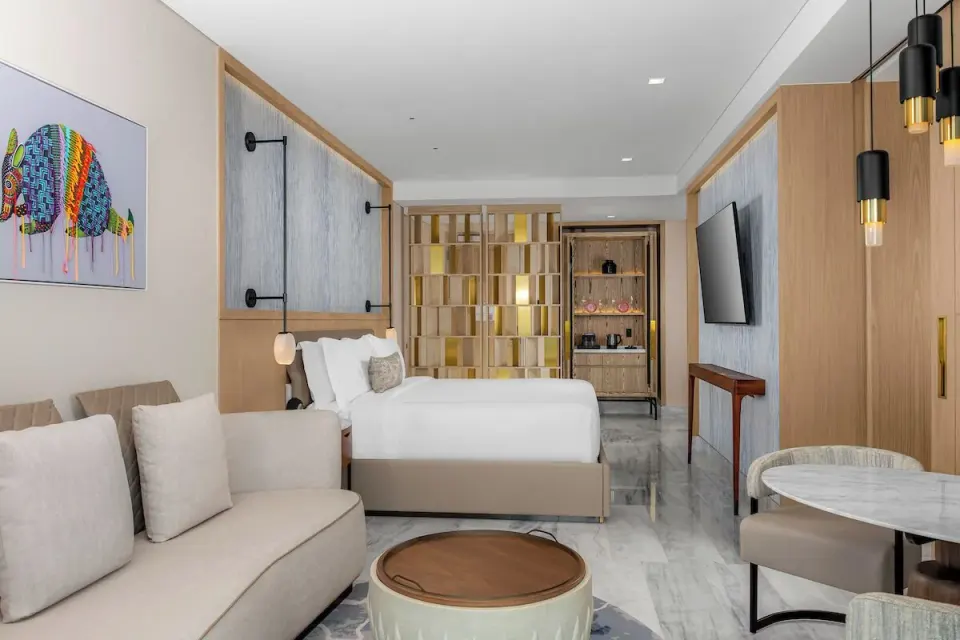 Accessible room with king bed, sofa, table, and wall TV at Waldorf Astoria Riviera Maya.