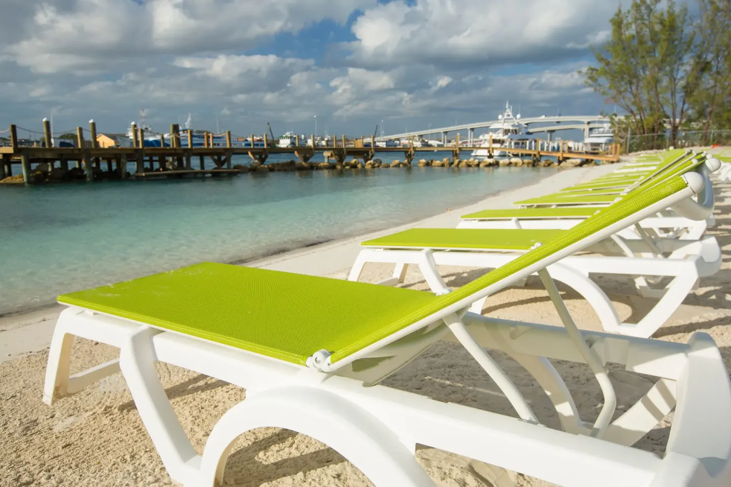 Green lounge chairs line the sandy beach at Warwick Paradise Island beside calm turquoise water.