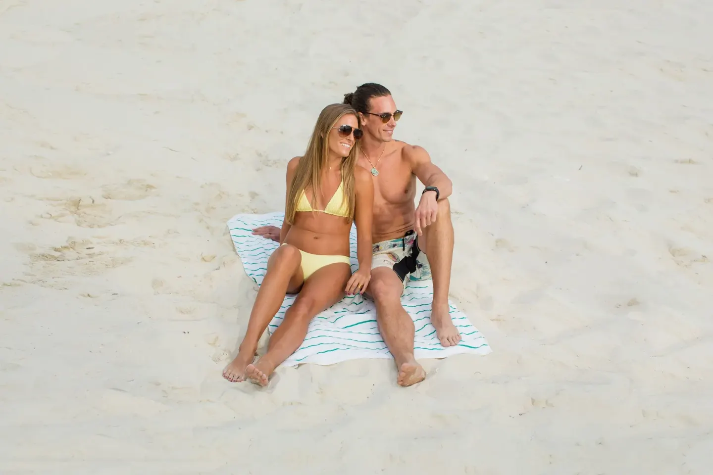A couple sits on a towel on the sandy beach at Warwick Paradise Island.