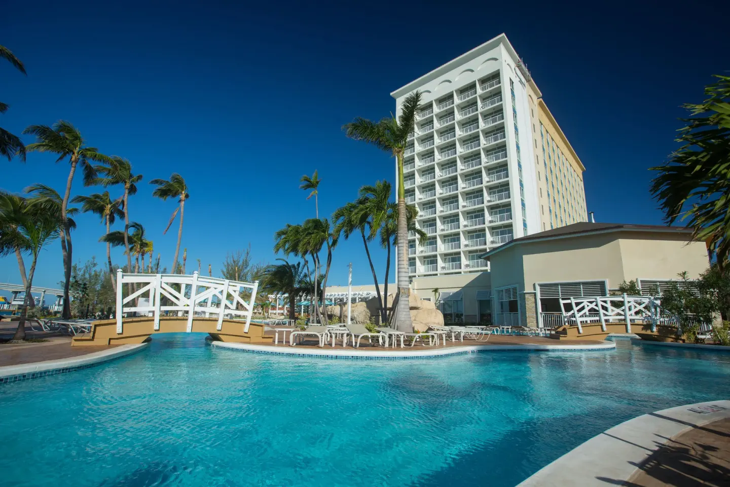 Curving pool, white bridge and palm trees below the tower at Warwick Paradise Island.