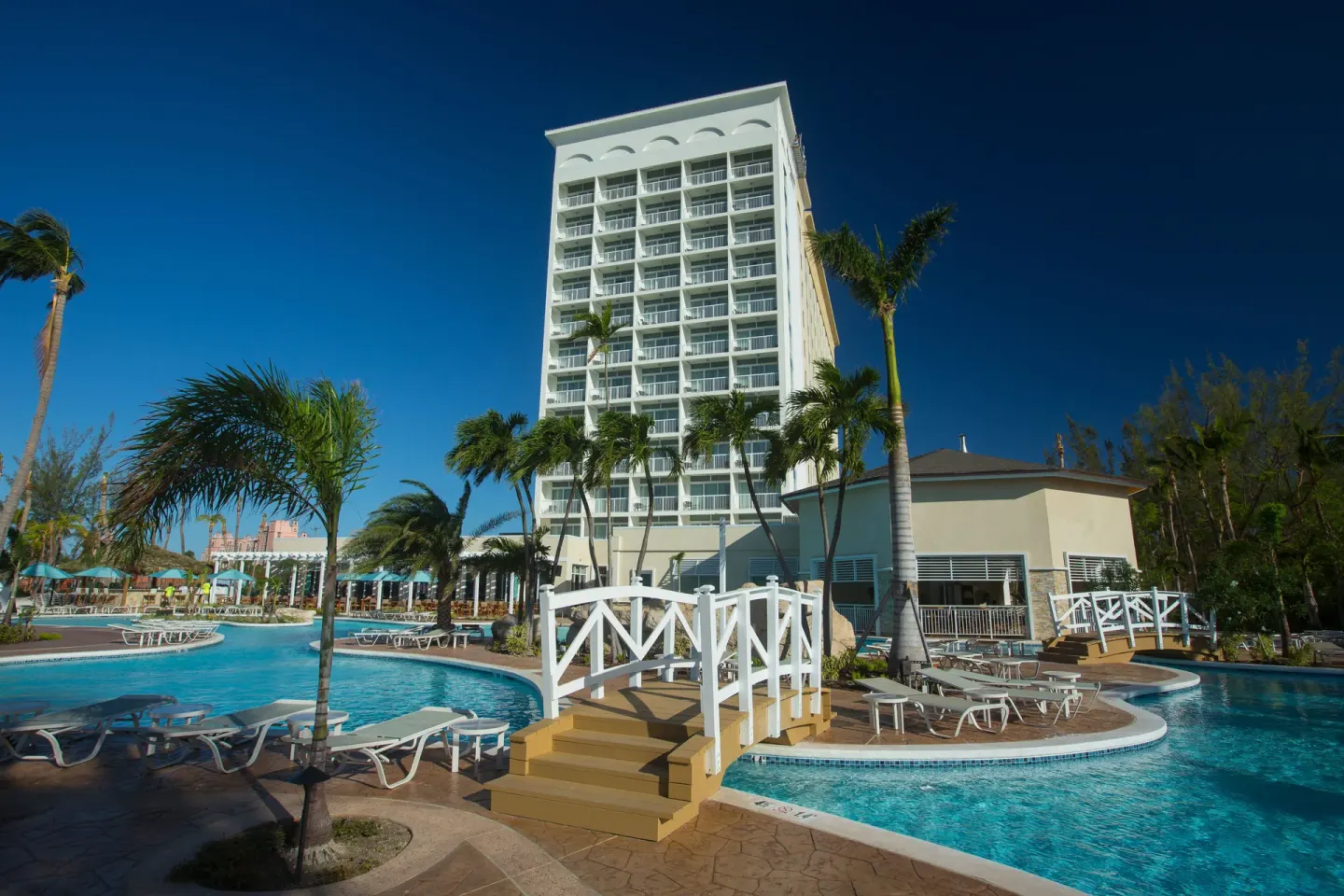 Pool deck, footbridge and hotel tower framed by palms at Warwick Paradise Island.