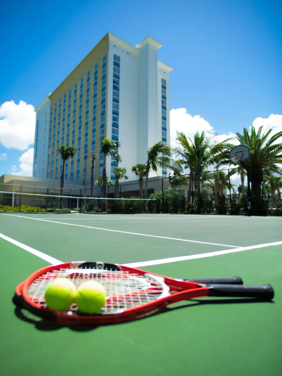 Tennis racquets and balls rest on the court with Warwick Paradise Island behind them.
